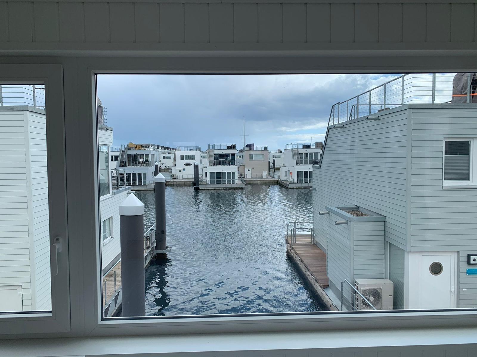 From the window, you can see a harbor with modern houses and water.