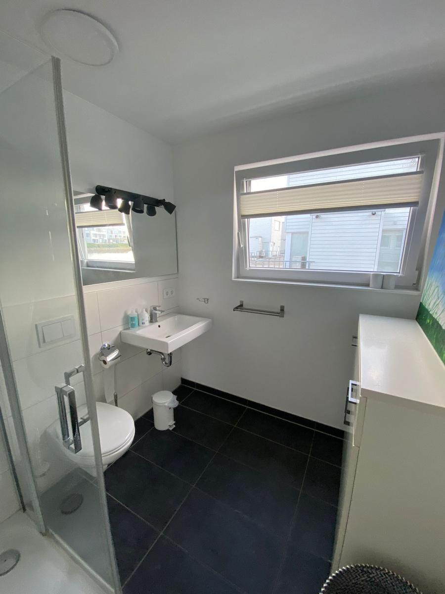 Bathroom with shower, sink, and toilet. Window with blinds.