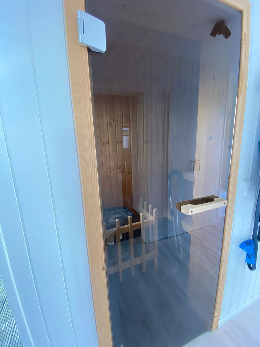 Sauna with wooden walls and glass door. Wooden bench and heater visible.