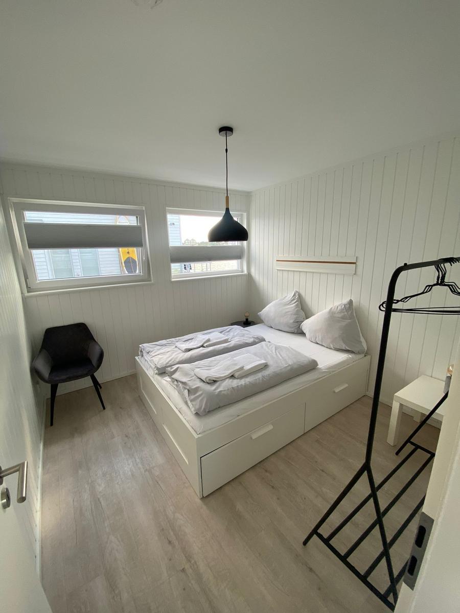 Bedroom with double bed, clothes rack, and two windows with blinds.
