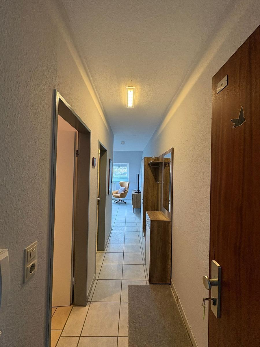 Flur mit Tür, Garderobe und Blick in Wohnzimmer mit Sessel.