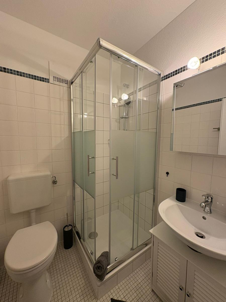 Badezimmer mit Dusche, Waschbecken und Toilette. Weiße Fliesen und Spiegelschrank.