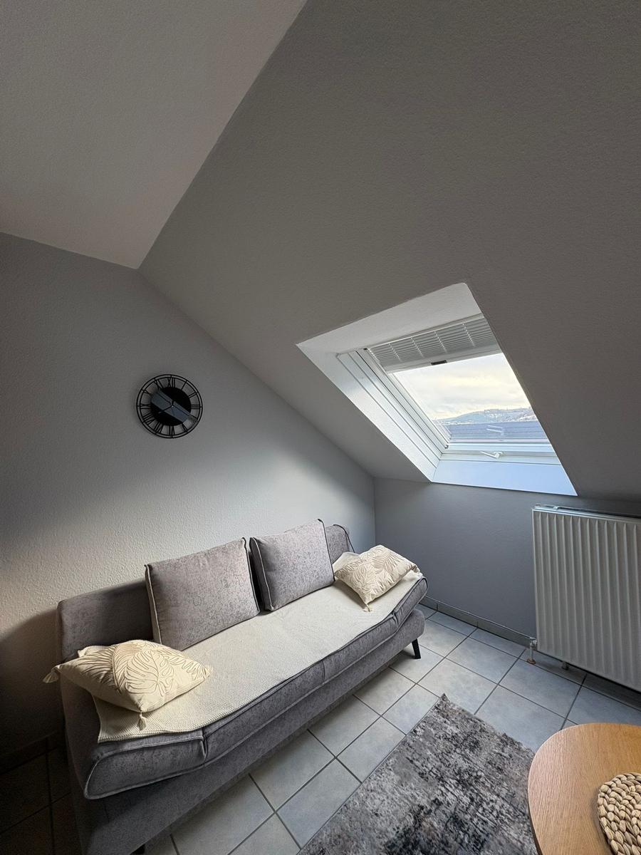 Ein Schlafzimmer mit Dachschrägen, Sofa, Fenster und Wanduhr.