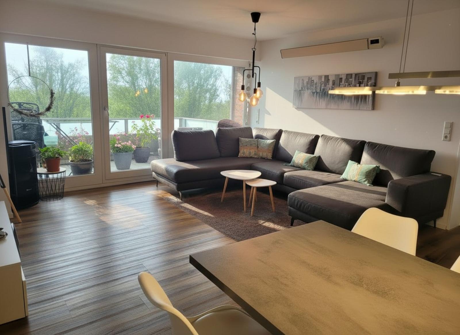 Wohnzimmer mit Ecksofa, Holzboden und Balkonansicht. Essbereich mit Tisch und Stühlen.