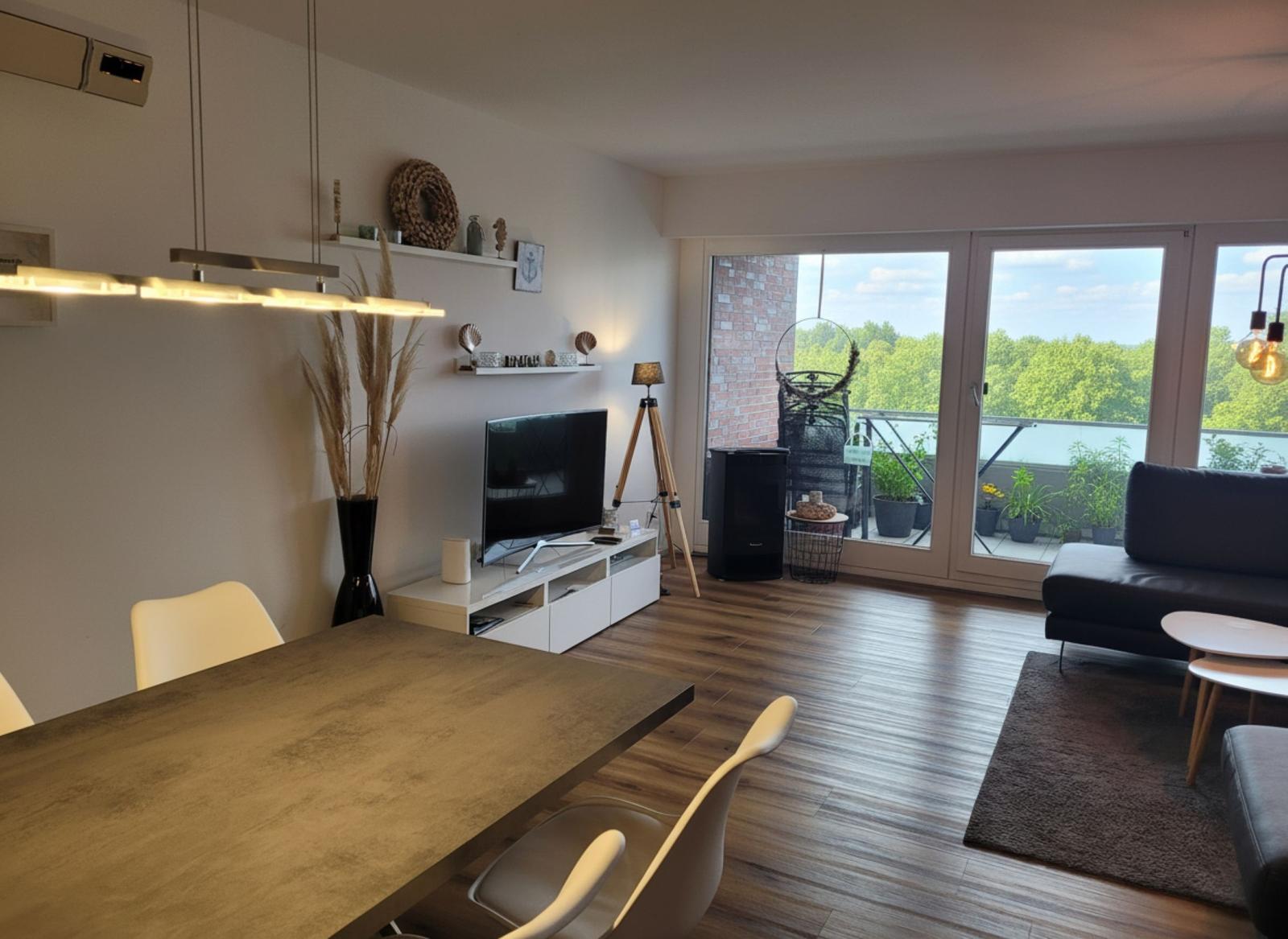 Wohn- und Essbereich mit Balkon, TV, Tisch und Stühlen sowie Pflanzen.
