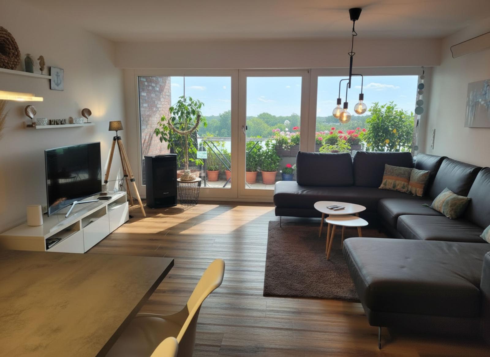 Wohnzimmer mit Sofa, TV und Balkon mit Pflanzen.
