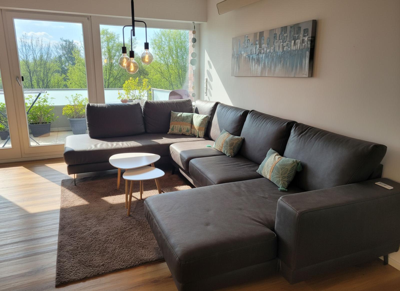 Ein Wohnzimmer mit einem großen Sofa, einem Tisch und einer Terrasse mit Blick auf Bäume.