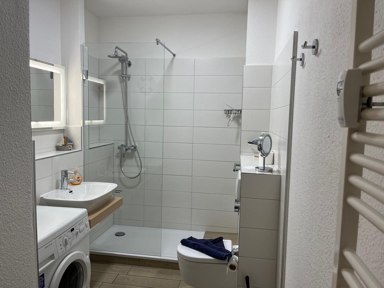 Badezimmer mit Dusche, Waschbecken, Toilette und Wärmeelement.