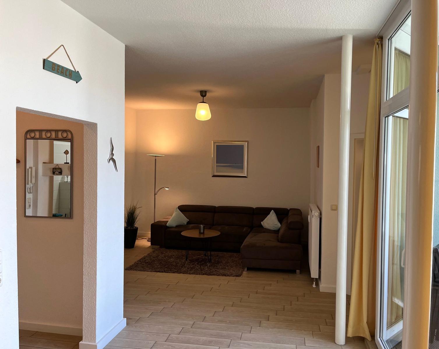 Wohnzimmer mit Sofa, Tisch und Wandbild. Durchgang zu Bad und Terrasse.
