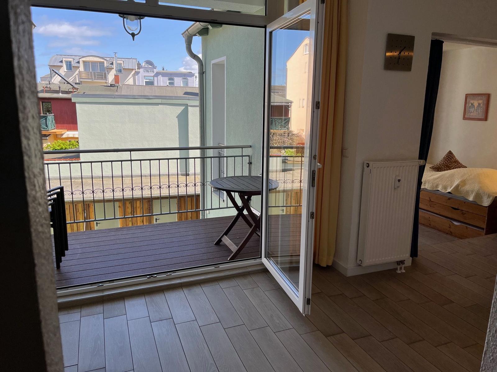 Terrasse mit Tisch und Blick auf Gebäude. Im Hintergrund ein Schlafzimmer mit Bett.