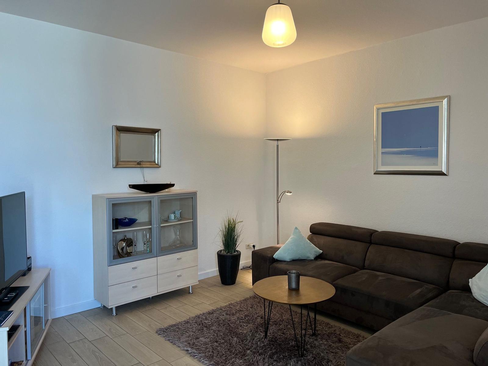 Wohnzimmer mit Sofa, Couchtisch, Fernseher und Glasvitrine.