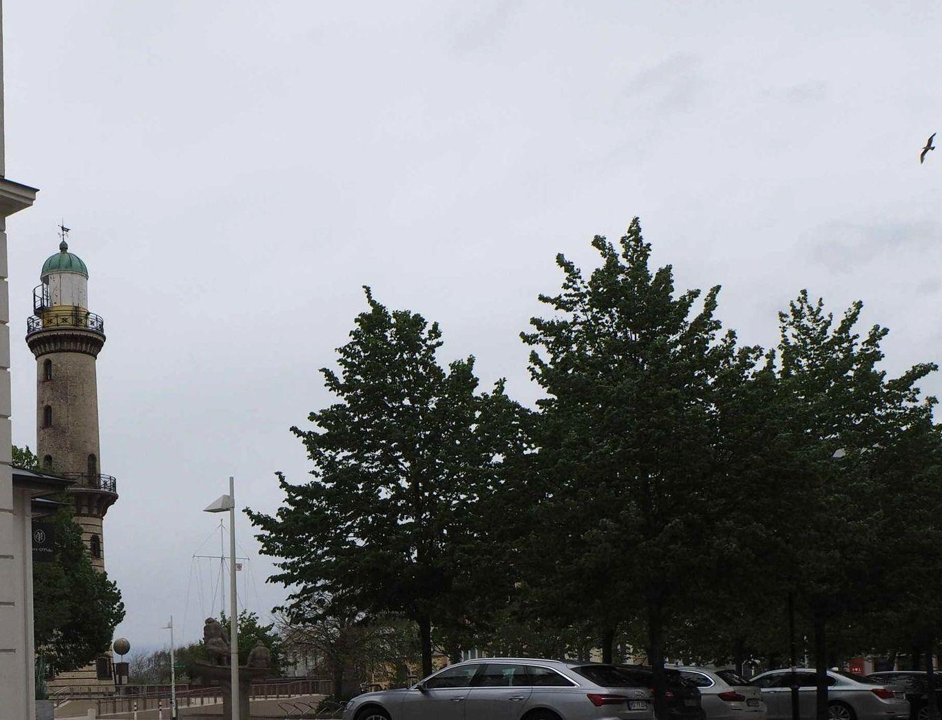 Hafenbecken mit Leuchtturm, Bäumen und parkenden Autos unter bewölktem Himmel.