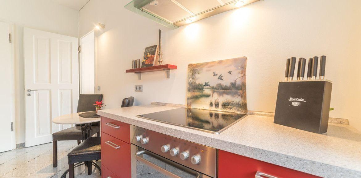 Küche mit roten Schränken, Kochfeld und Messerblock. Tisch und Stühle im Hintergrund.