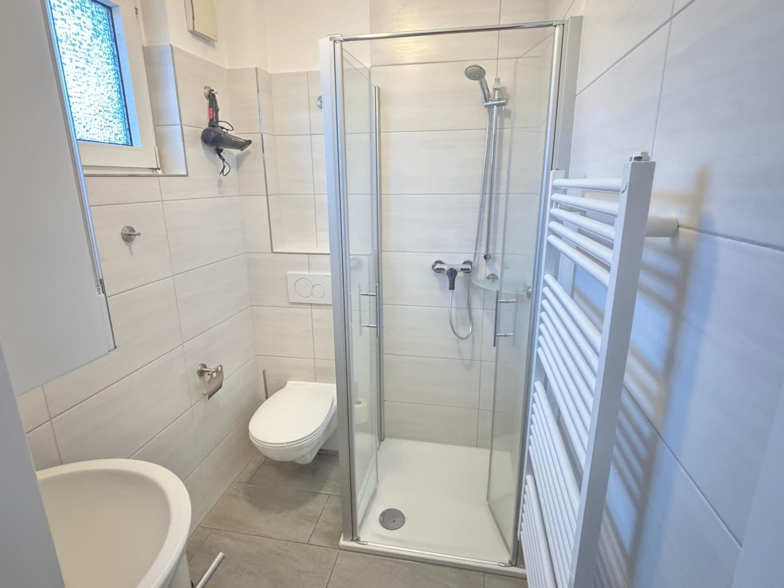 Badezimmer mit Dusche, Toilette und Waschbecken. Fenster mit Mosaikglas.