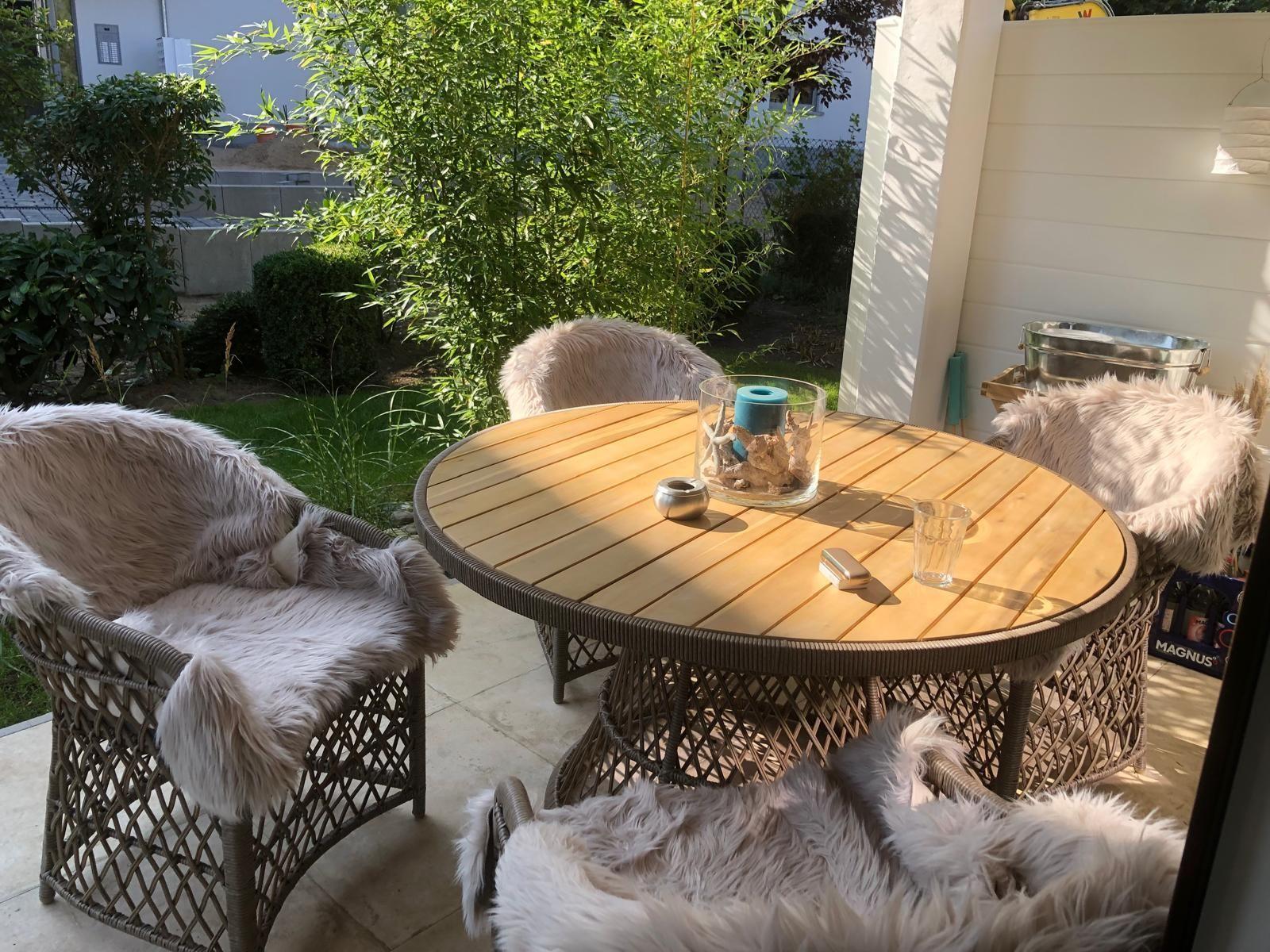 Runder Holztisch mit vier Stühlen, bedeckt mit flauschigen Decken im Garten.