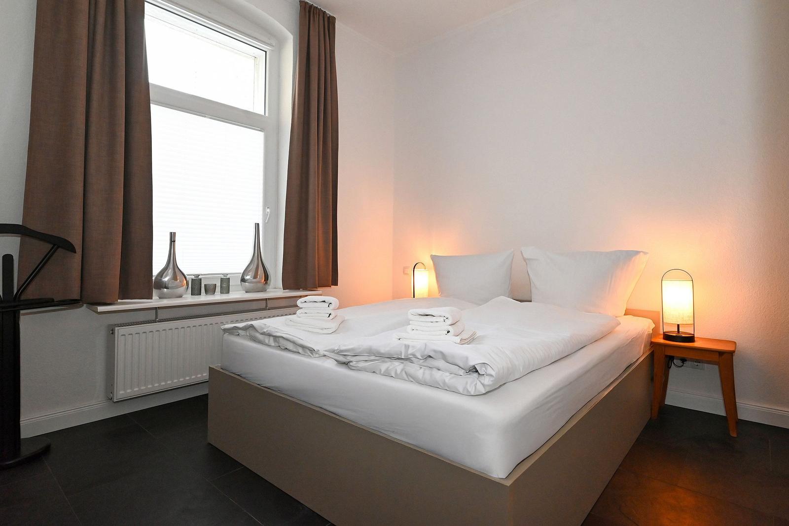 Schlafzimmer mit Bett, Nachttisch und Fenster mit Vorhängen.