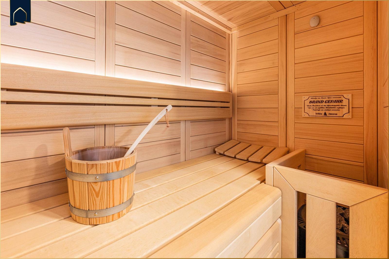Sauna mit Holzbank, Eimer und Warnschild an der Wand.