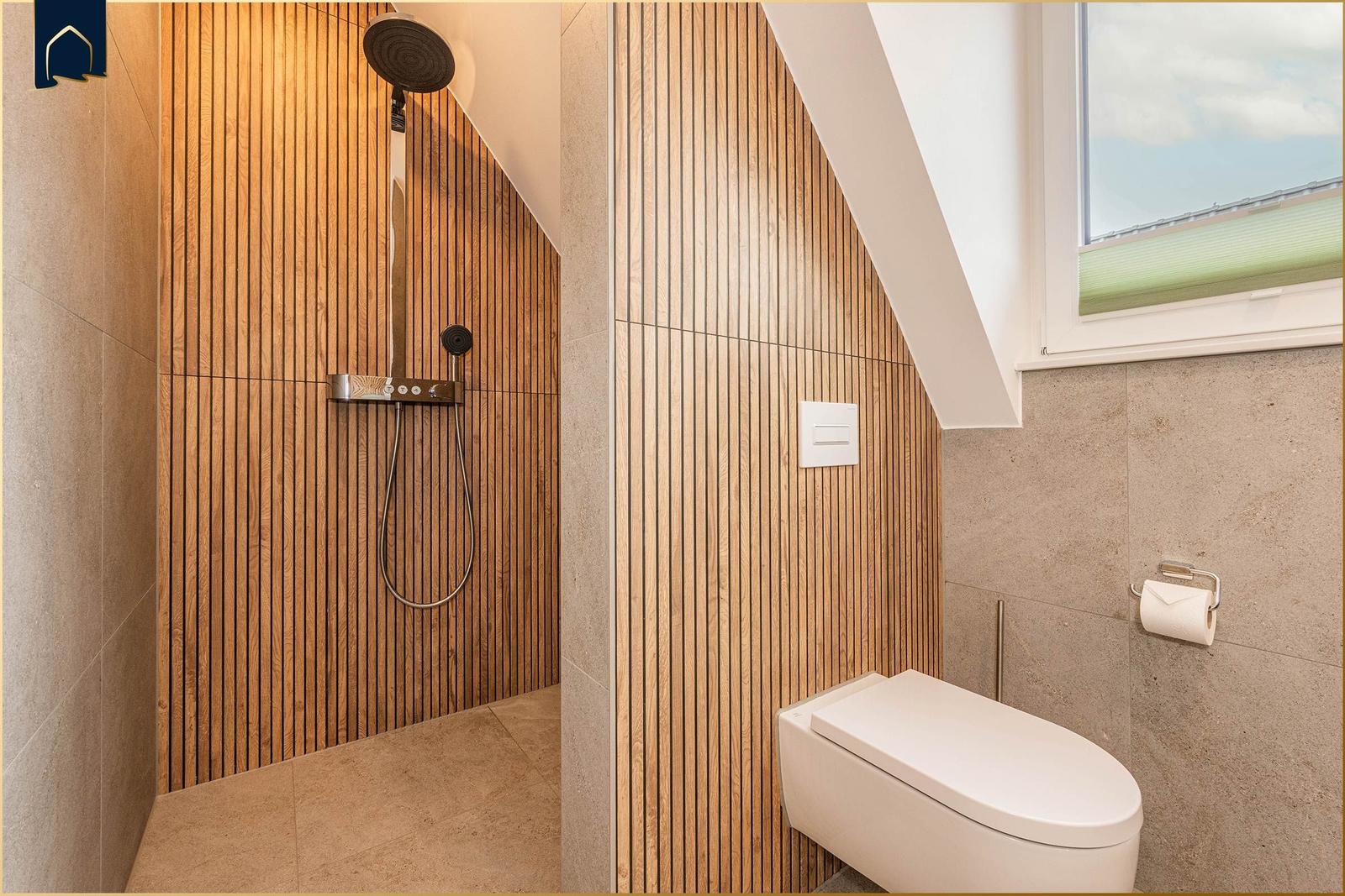 Dusche mit Holzwand und Toilette unter Dachschrägen mit Fenster.