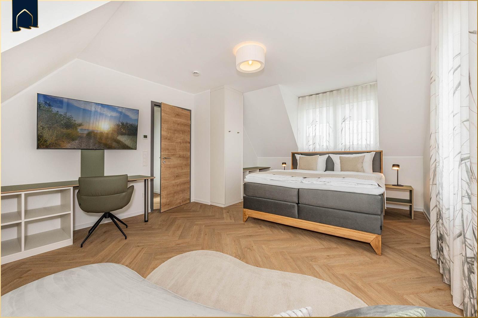 Schlafzimmer mit Bett, Schreibtisch, TV und Holzboden.