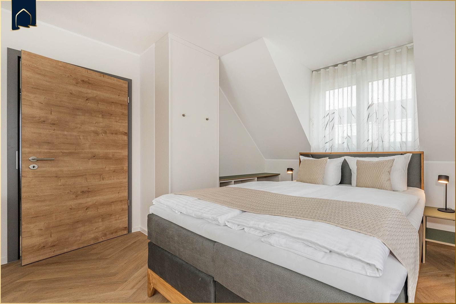 Schlafzimmer mit Doppelbett, Holztür und Fenster mit Vorhängen.