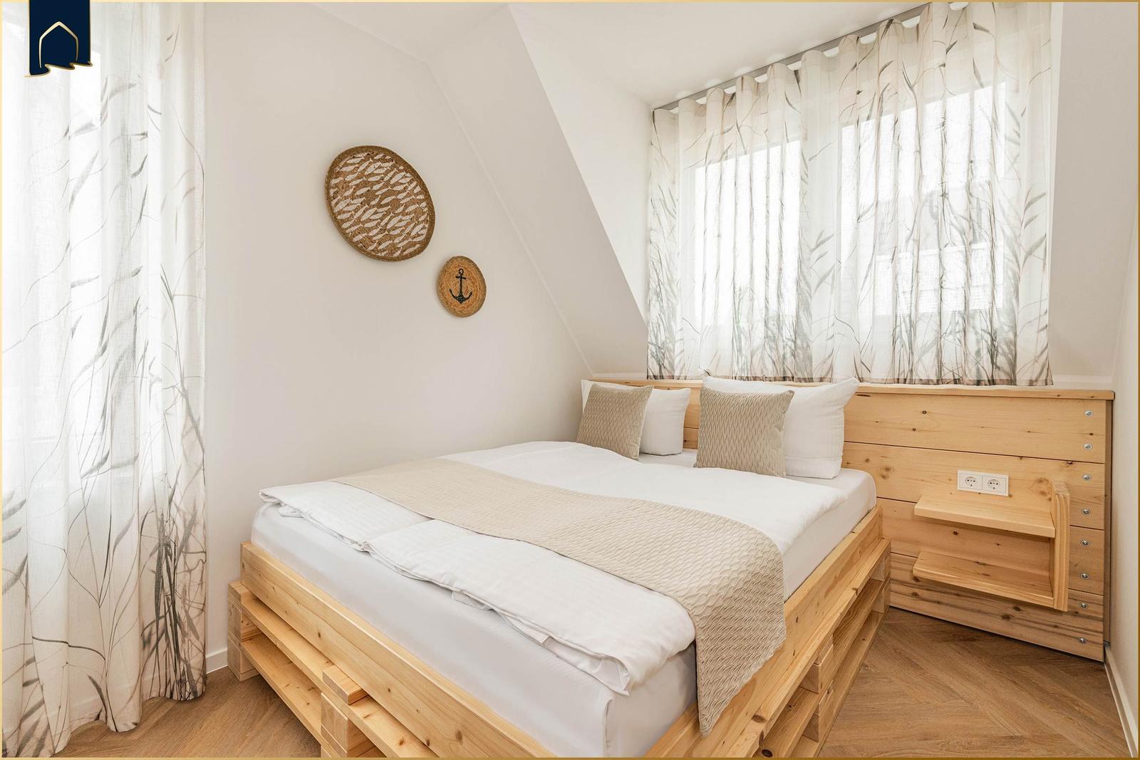 Schlafzimmer mit Holzbett, Fenster mit Vorhängen und Wanddekoration.