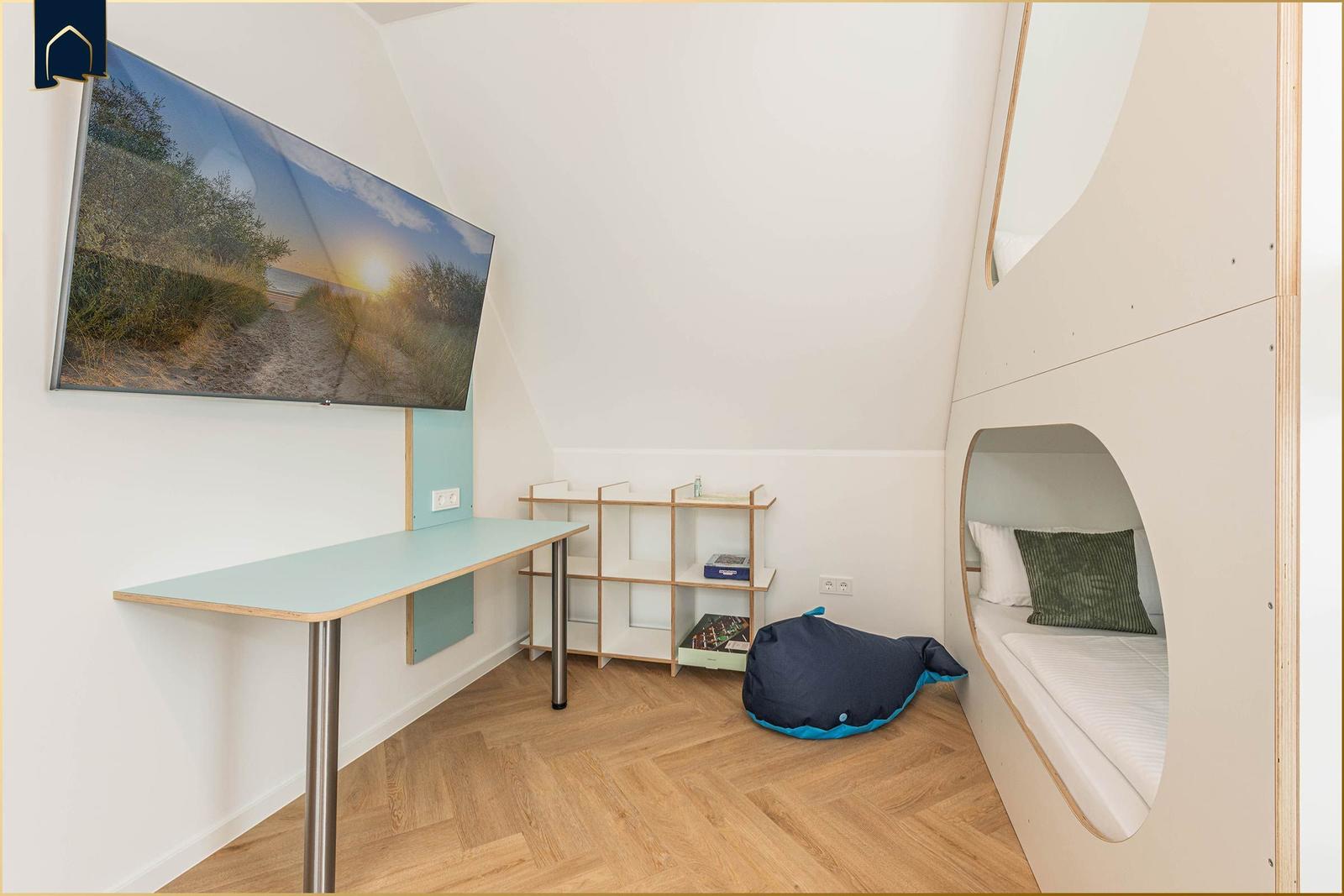 Ein Zimmer mit Schreibtisch, Regal und Schlafplatz in einem runden Kasten.