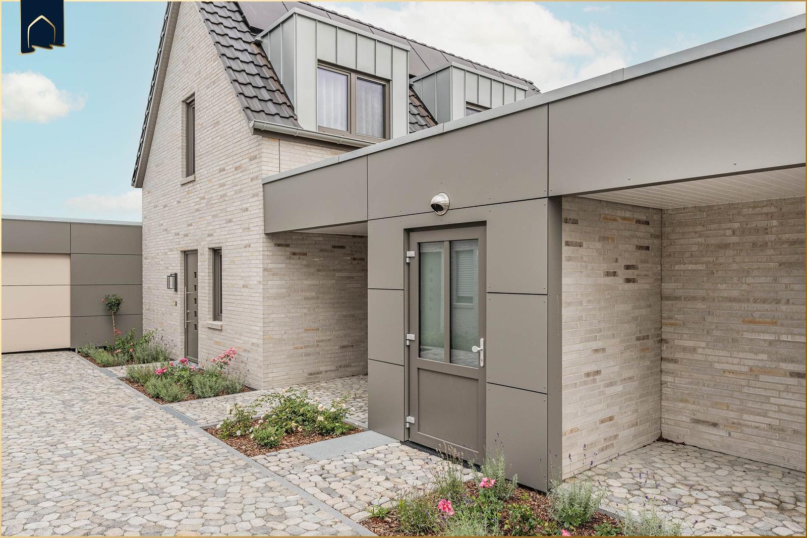 Moderne Villa mit Steinmauer, Eingangstür und gepflastertem Hof mit Blumenbeeten.