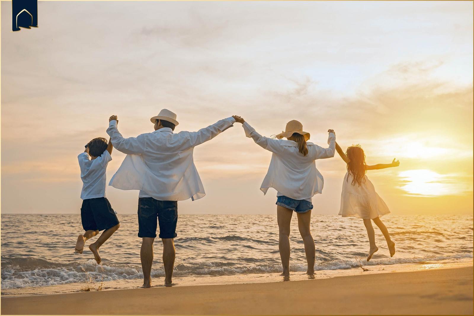 Eine Familie springt am Strand im Sonnenuntergang Hand in Hand.