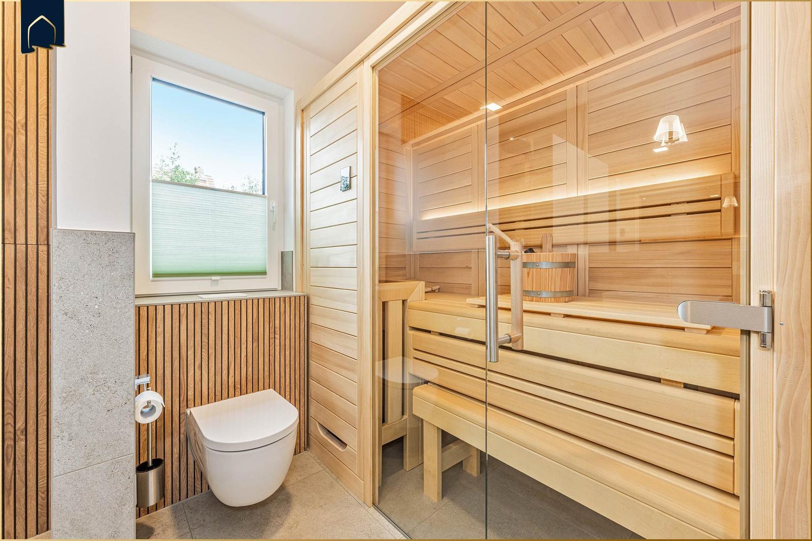 Duschbad mit Sauna und Toilette. Holzverkleidung und Glasfront sichtbar.