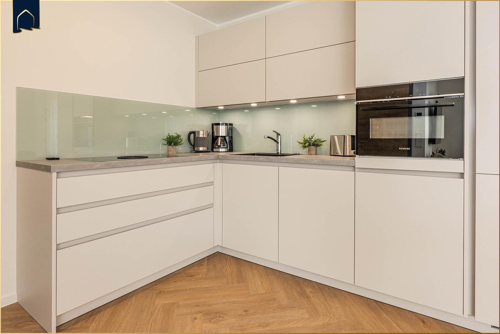 Moderne Küche mit weißen Schränken, Glasrückwand und integriertem Ofen.