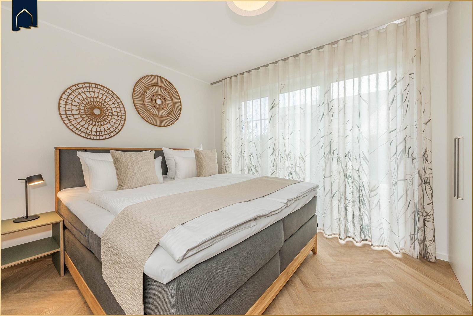 Schlafzimmer mit Bett, Nachttisch und Fenster mit Vorhängen.