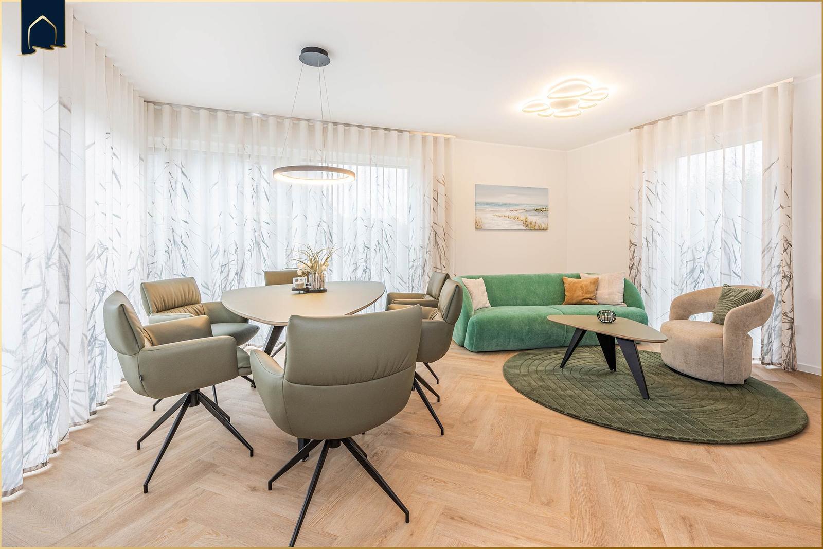 Wohn- und Essbereich mit grünem Sofa, runden Tisch und hellen Holzboden.