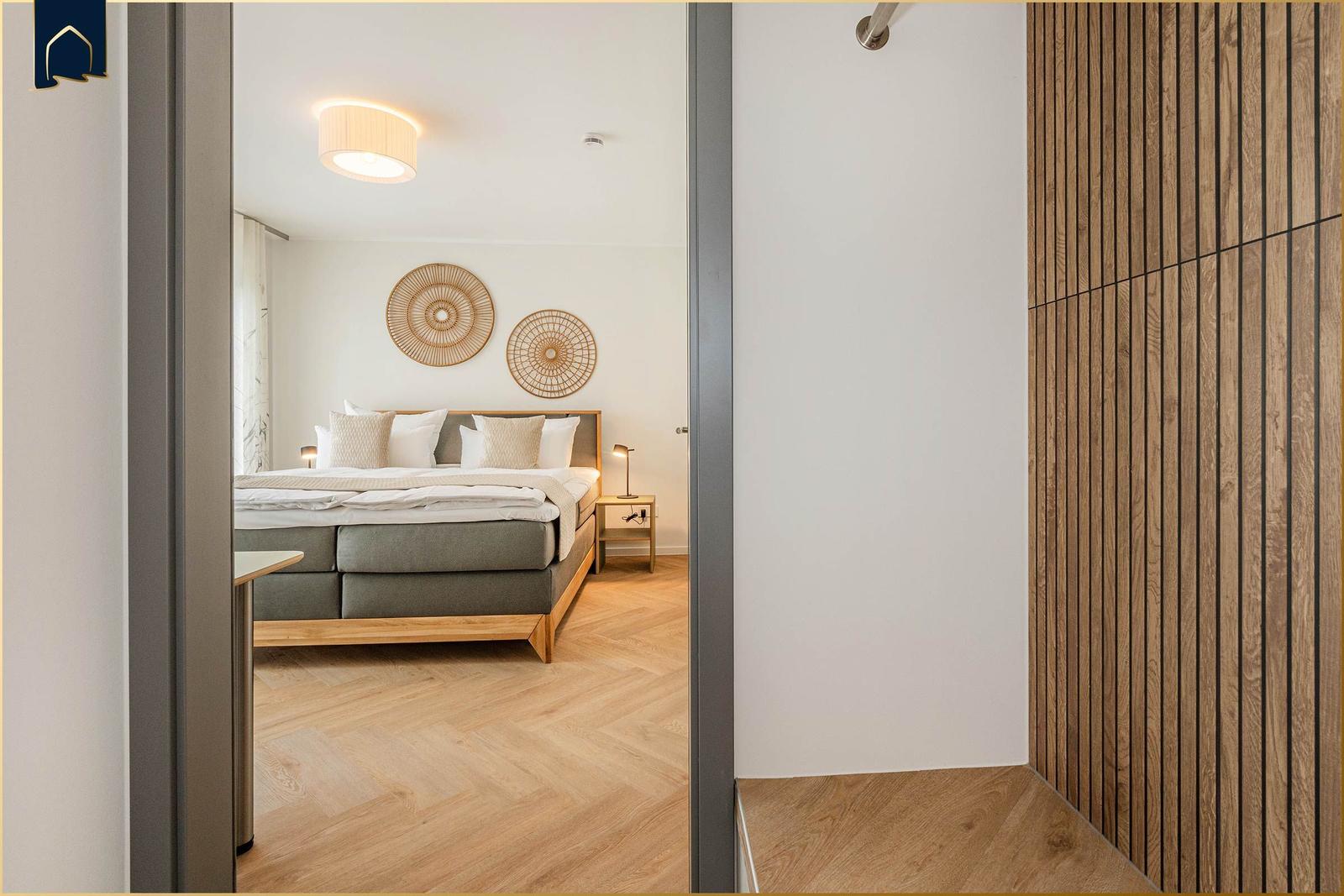 Schlafzimmer mit Bett, Nachttisch und Holzboden. An der Wand hängen zwei runde Dekorationen.