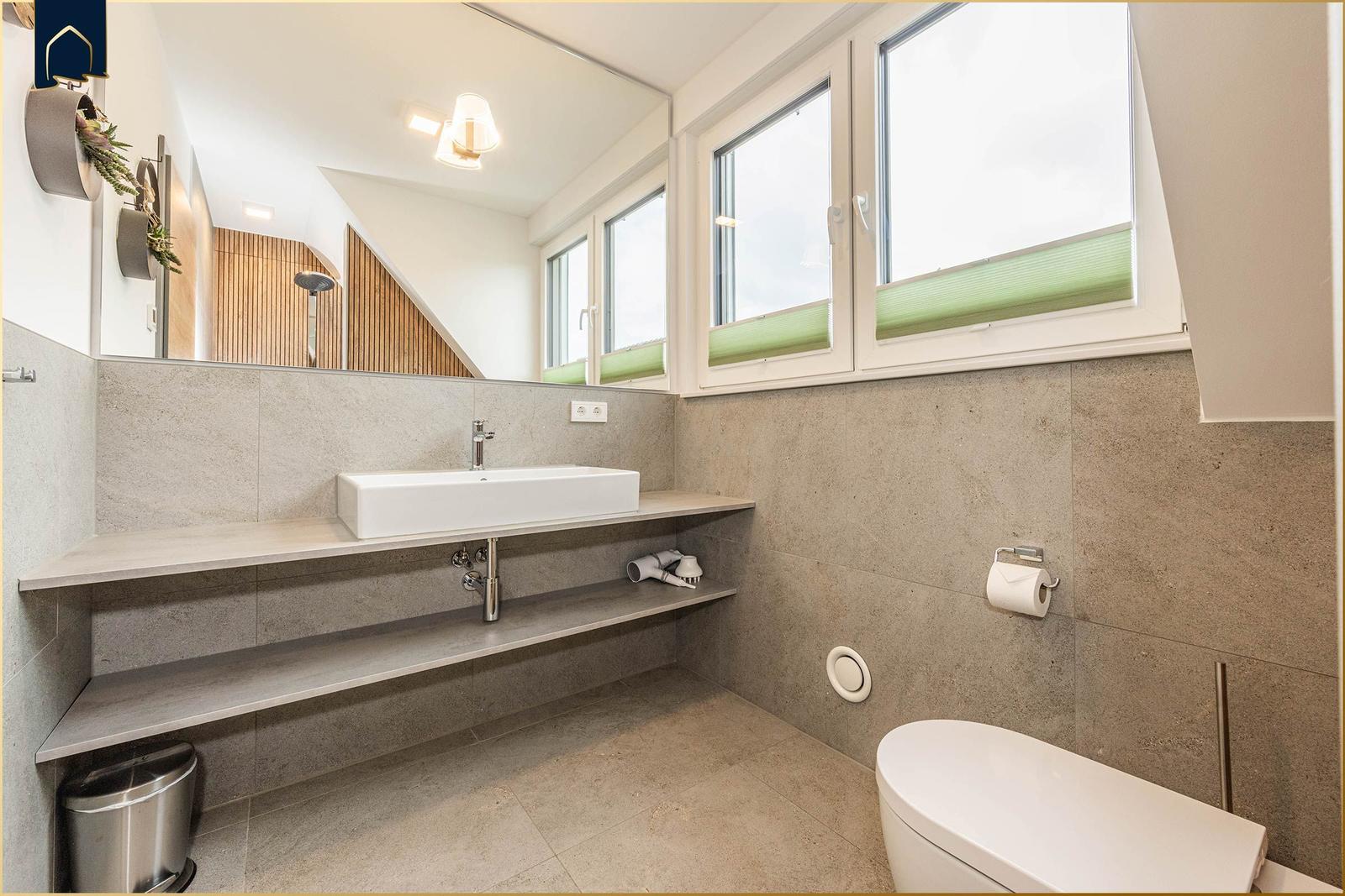 Badezimmer mit Waschbecken, Toilette und Fenstern.