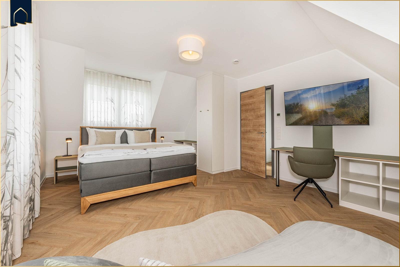 Schlafzimmer mit Doppelbett, Schreibtisch und TV. Holzboden und Dachschräge.