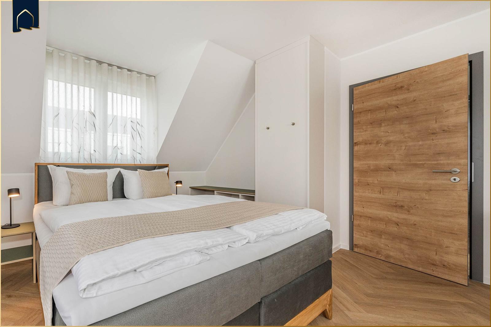 Schlafzimmer mit Doppelbett, Holztür und Fenster mit Vorhängen.