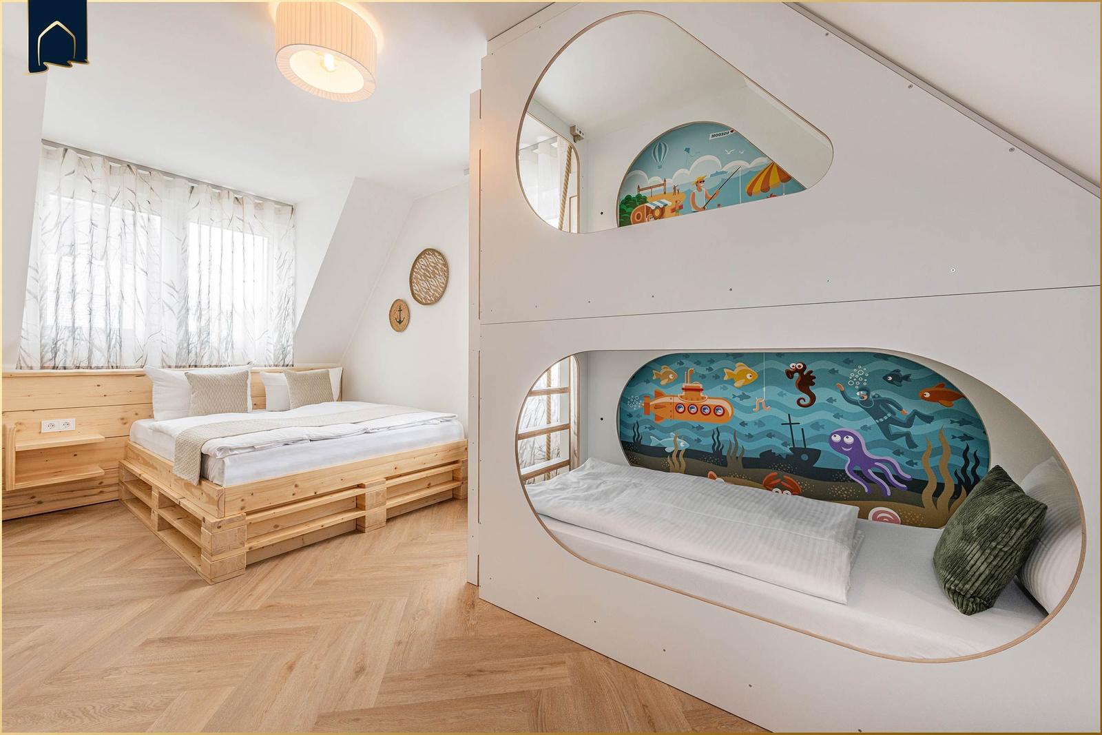 Zimmer mit Doppelbett und zwei Kinderbetten mit Meeresthemen.