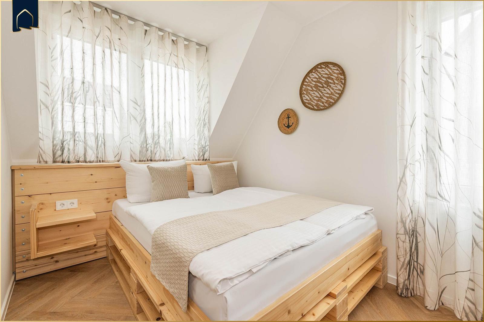 Schlafzimmer mit Holzbett, Fenster mit Vorhängen und Wanddekoration.