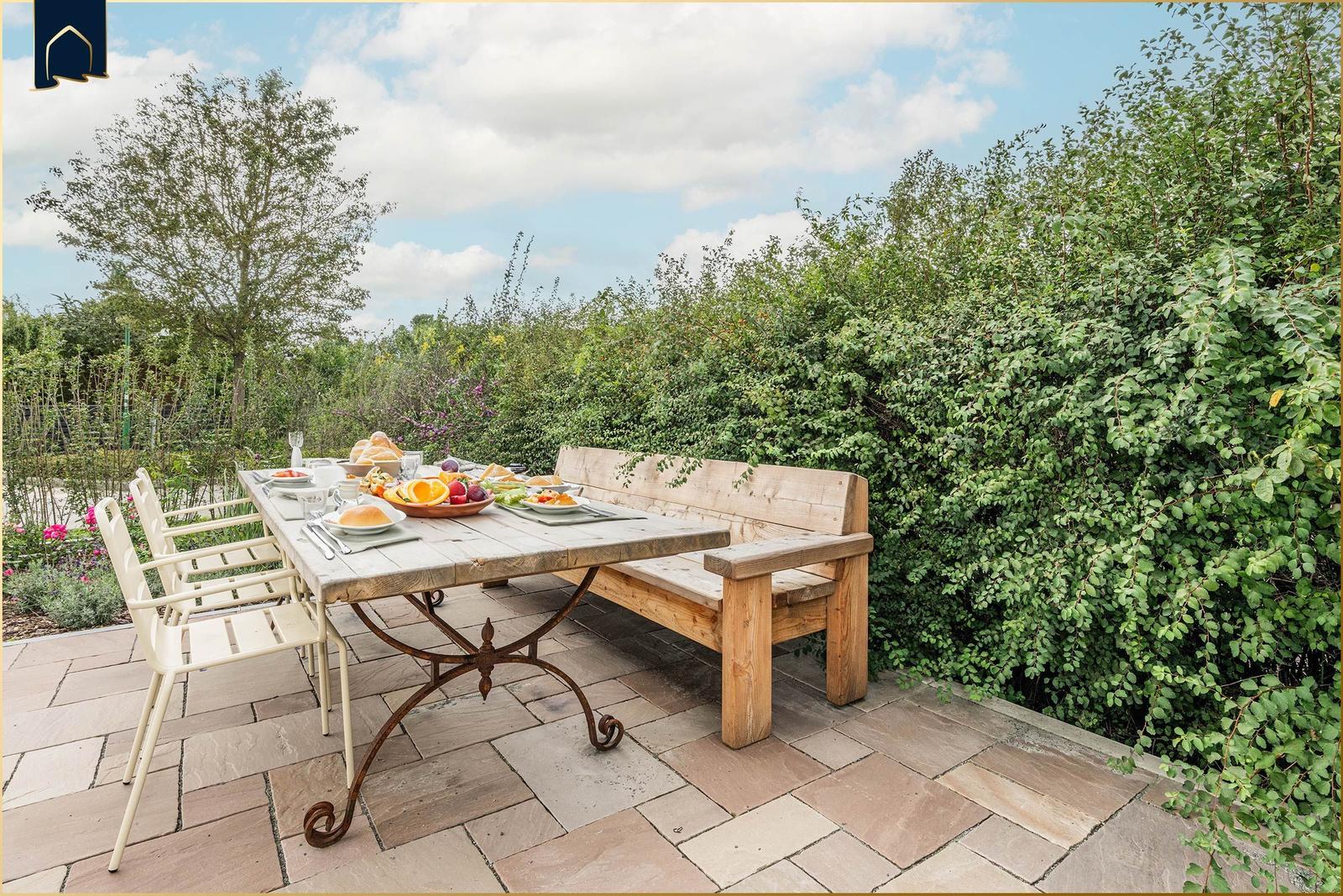 Terrasse mit Holztisch, Bänken und Stühlen. Frühstückstablett mit Obst und Brot.