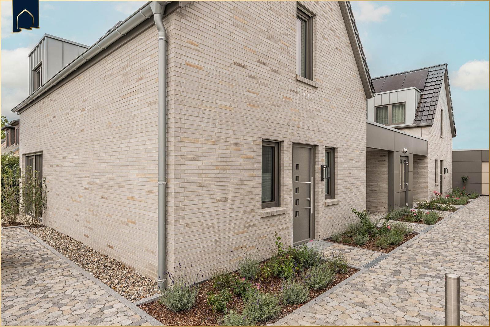 Moderne Villa mit Steinmauer und gepflastertem Hof. Eingangstür und Fenster sind sichtbar.