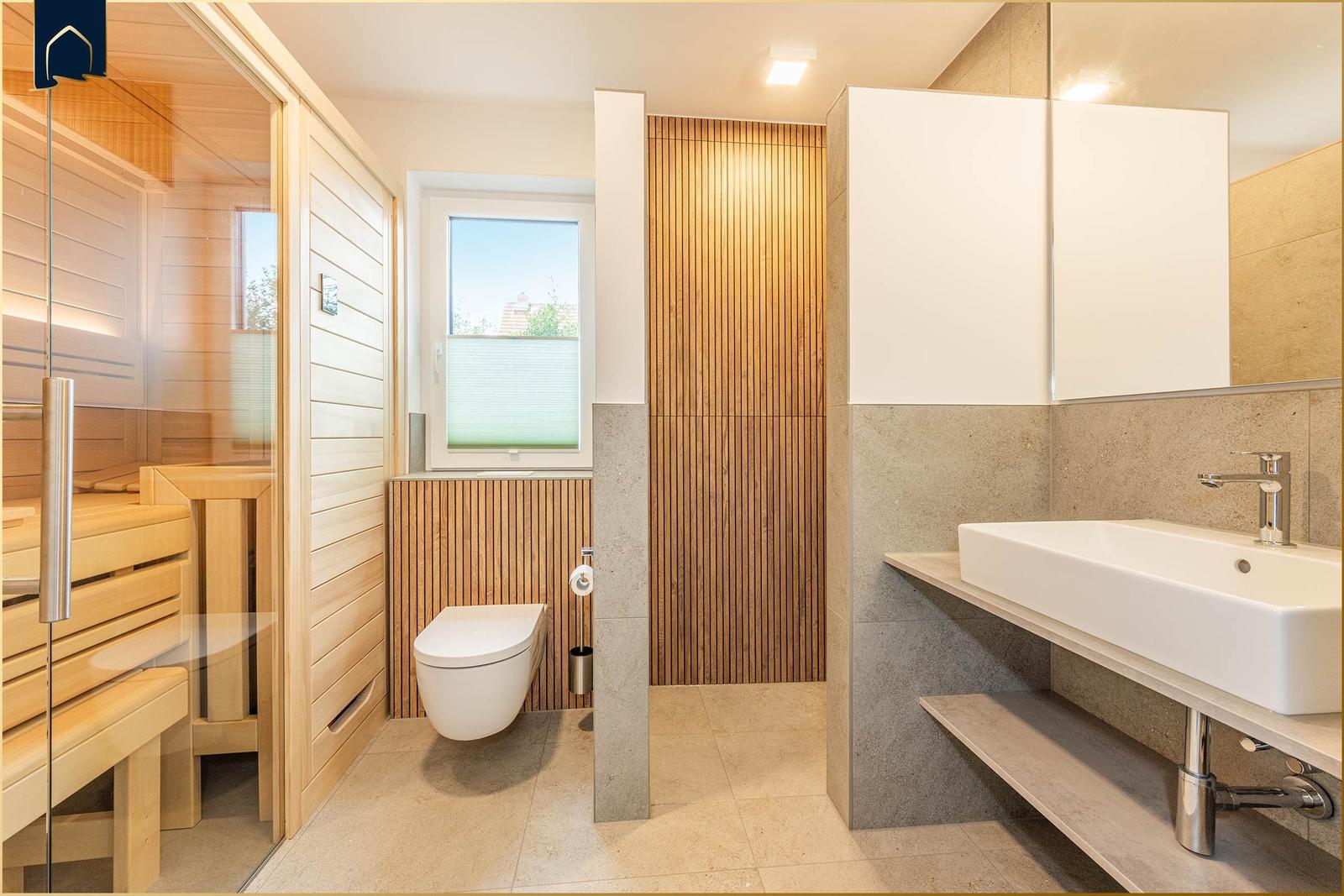 Bad mit Dusche, WC und Waschbecken. Holzwand und Fenster sichtbar.