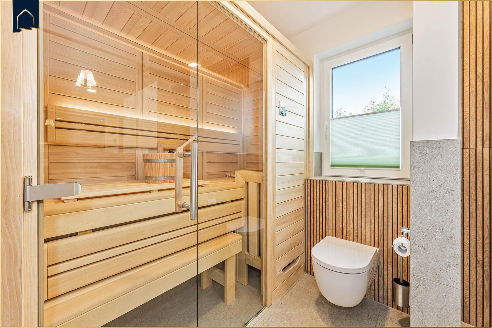 Sauna mit Holzbank und Eingangstür. Neben dem WC befindet sich ein Fenster.