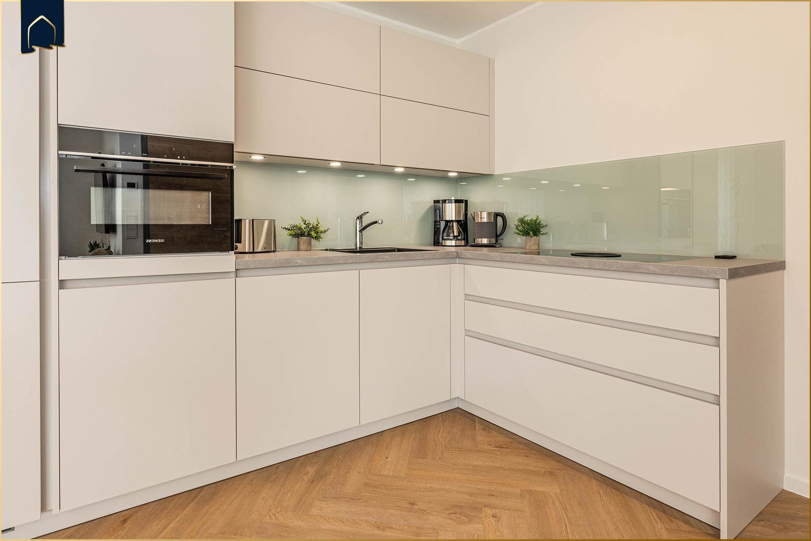 Moderne Küche mit hellen Schränken, Edelstahlgeräten und Holzboden.