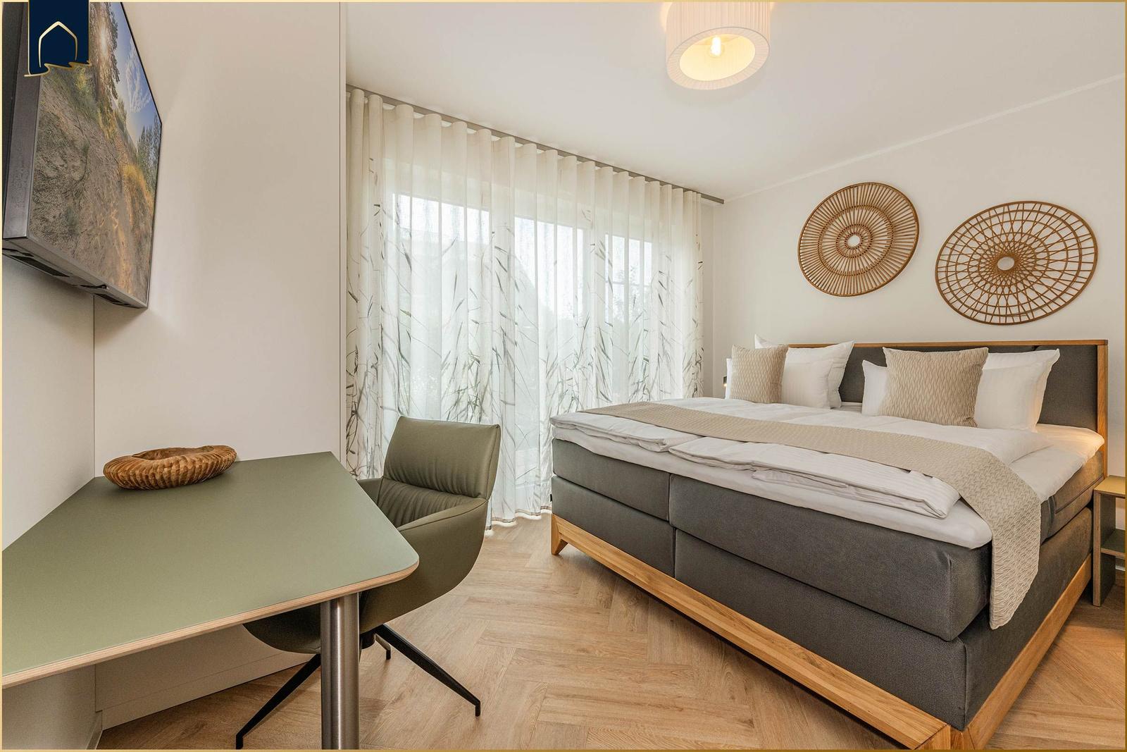 Schlafzimmer mit Bett, Schreibtisch und TV. Holzfußboden und weiße Wände.