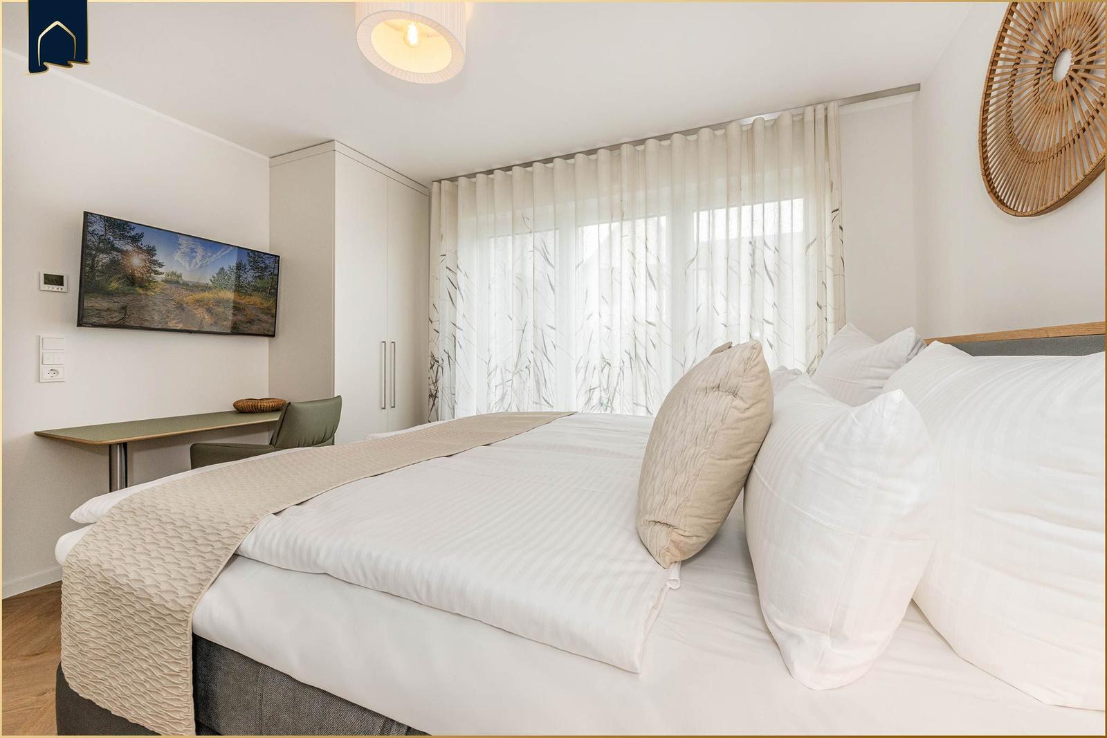 Schlafzimmer mit Bett, TV und Fenster mit Vorhängen.