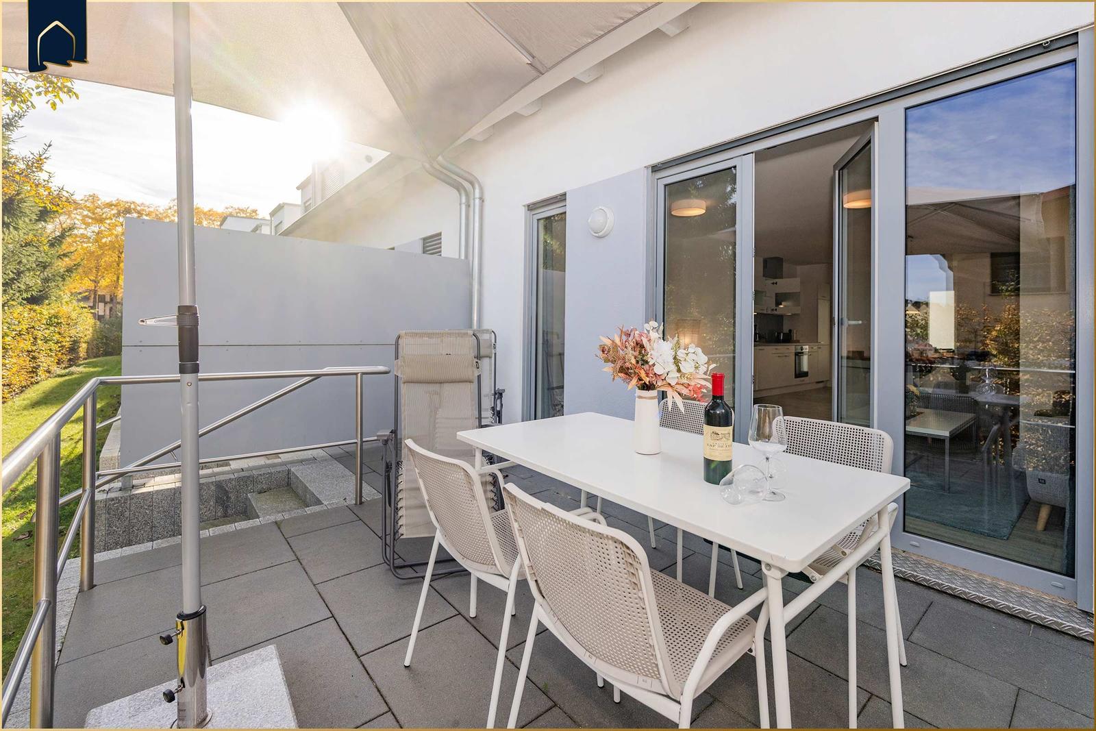 Terrasse mit Tisch, Stühlen und Sonnenschutz. Durchgang zur Küche sichtbar.