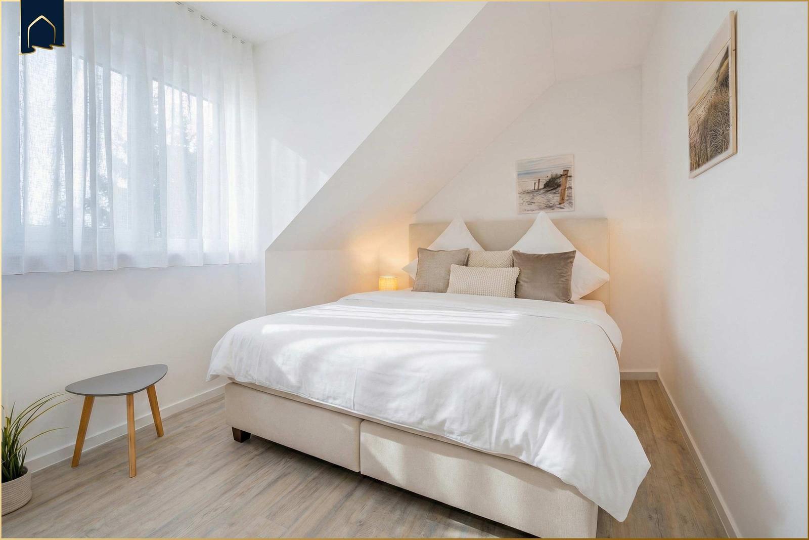 Schlafzimmer mit Dachschräge, Bett, Fenster und Wandbild.