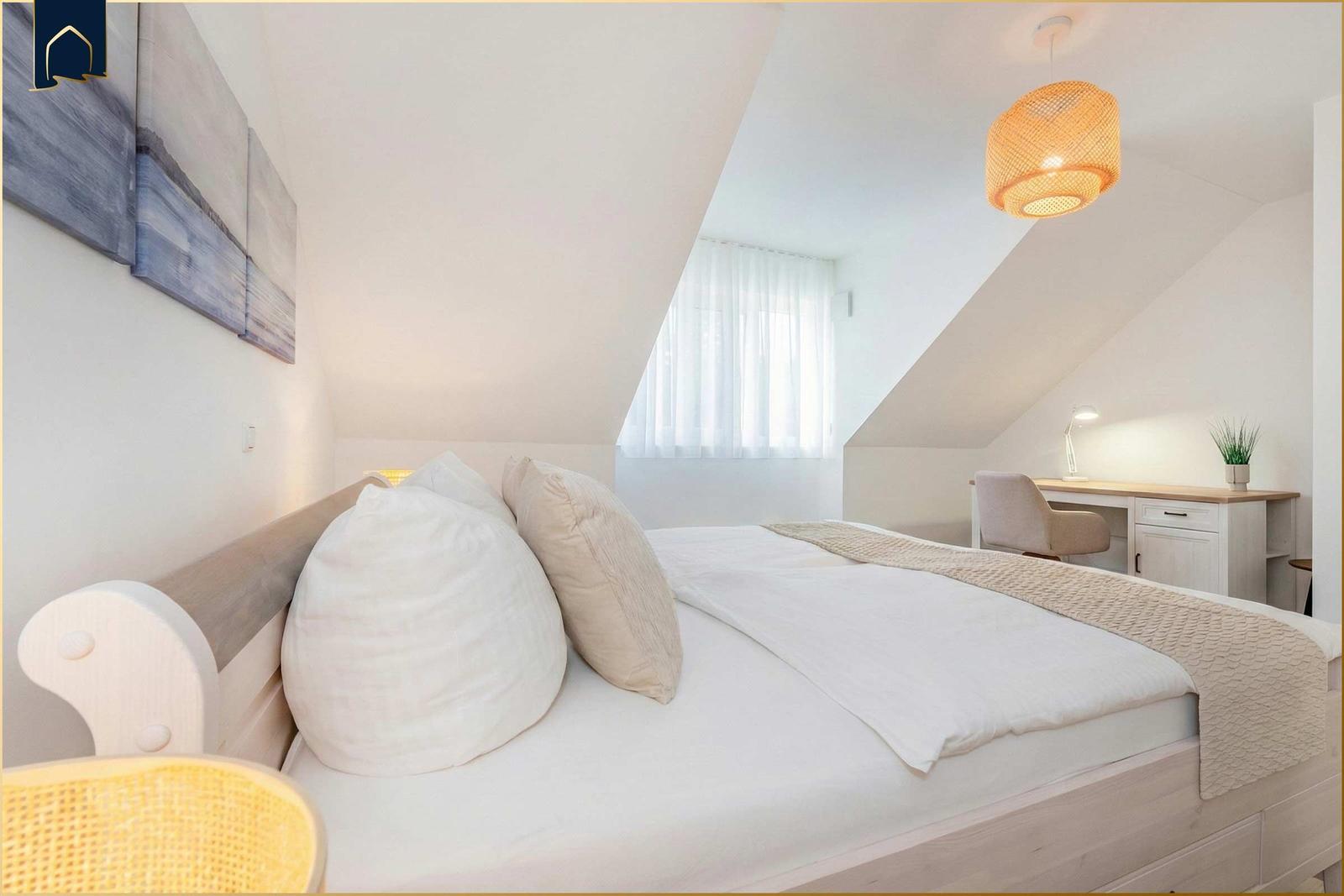 Schlafzimmer mit Dachschrägen, Bett, Schreibtisch und Lampe.