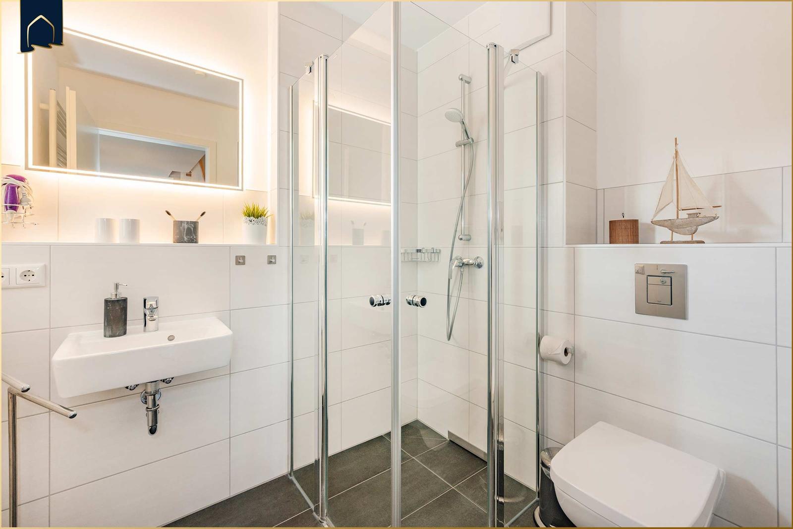 Badezimmer mit Dusche, Waschbecken und Toilette. Dekoration: Segelbootmodell.