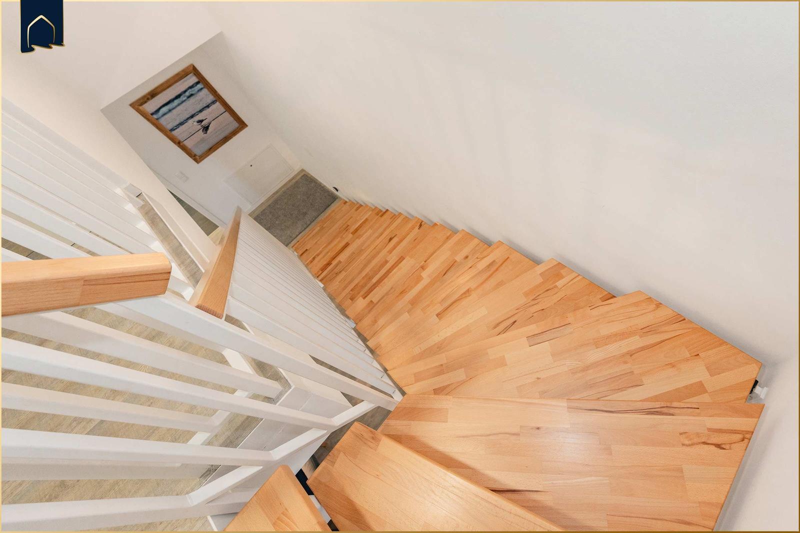 Holztreppe mit weißem Geländer führt nach oben. Wandbild mit Strandmotiv über dem Treppenhaus.